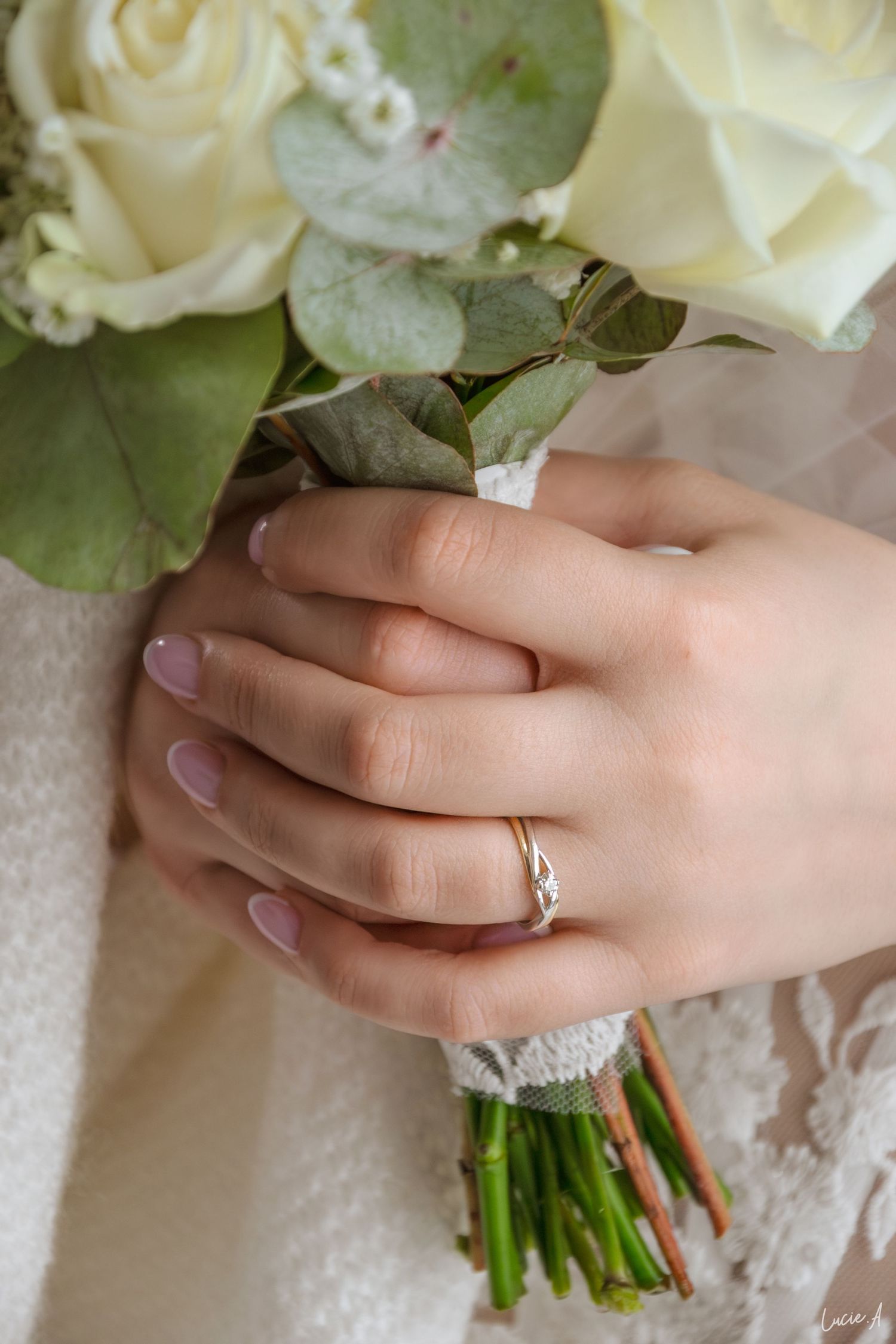 La mariée tient un bouquet de roses blanches, arbore une élégante bague de fiançailles en or et une manucure nude.