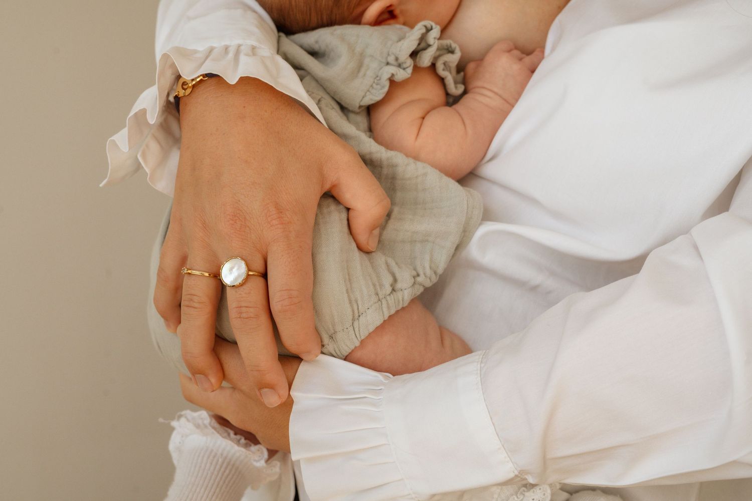 Two parents cradling a newborn baby wrapped in a soft green muslin cloth, wearing gold rings and white clothing.