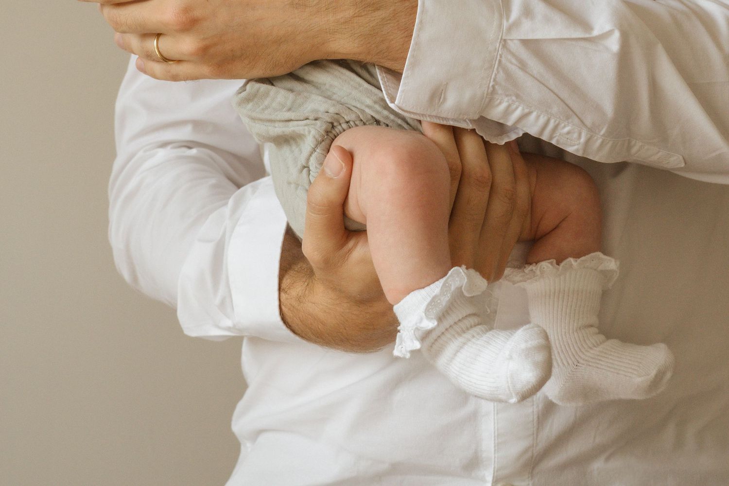 Adult in white shirt gently holding a newborn baby, showcasing tender parental bonding moment.