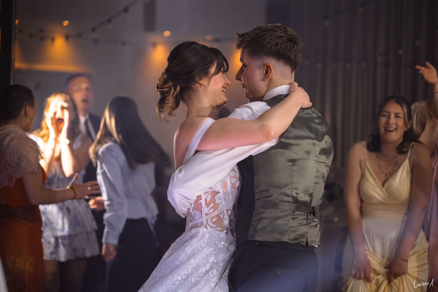 Les mariés partagent leur première danse entourés d'invités joyeux lors d'une réception de mariage chaleureusement éclairée.