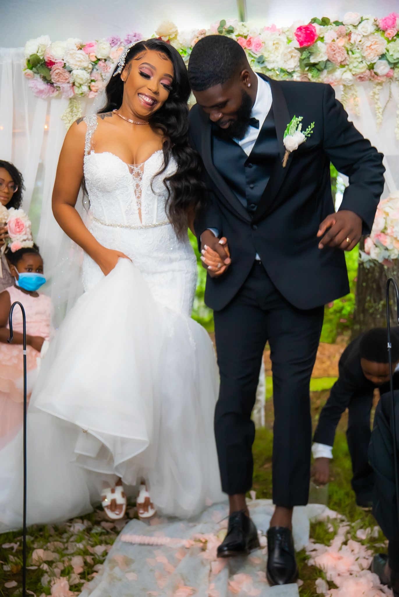 Smiling bride in white mermaid gown and groom in black tux celebrate at wedding ceremony.