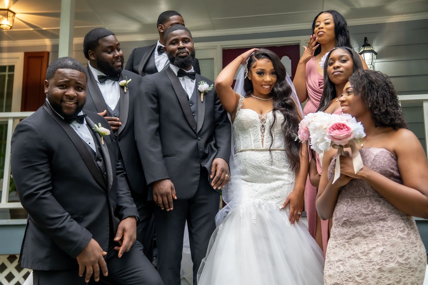 Wedding party poses on porch steps with bride in white gown and bridesmaids in pink dresses.