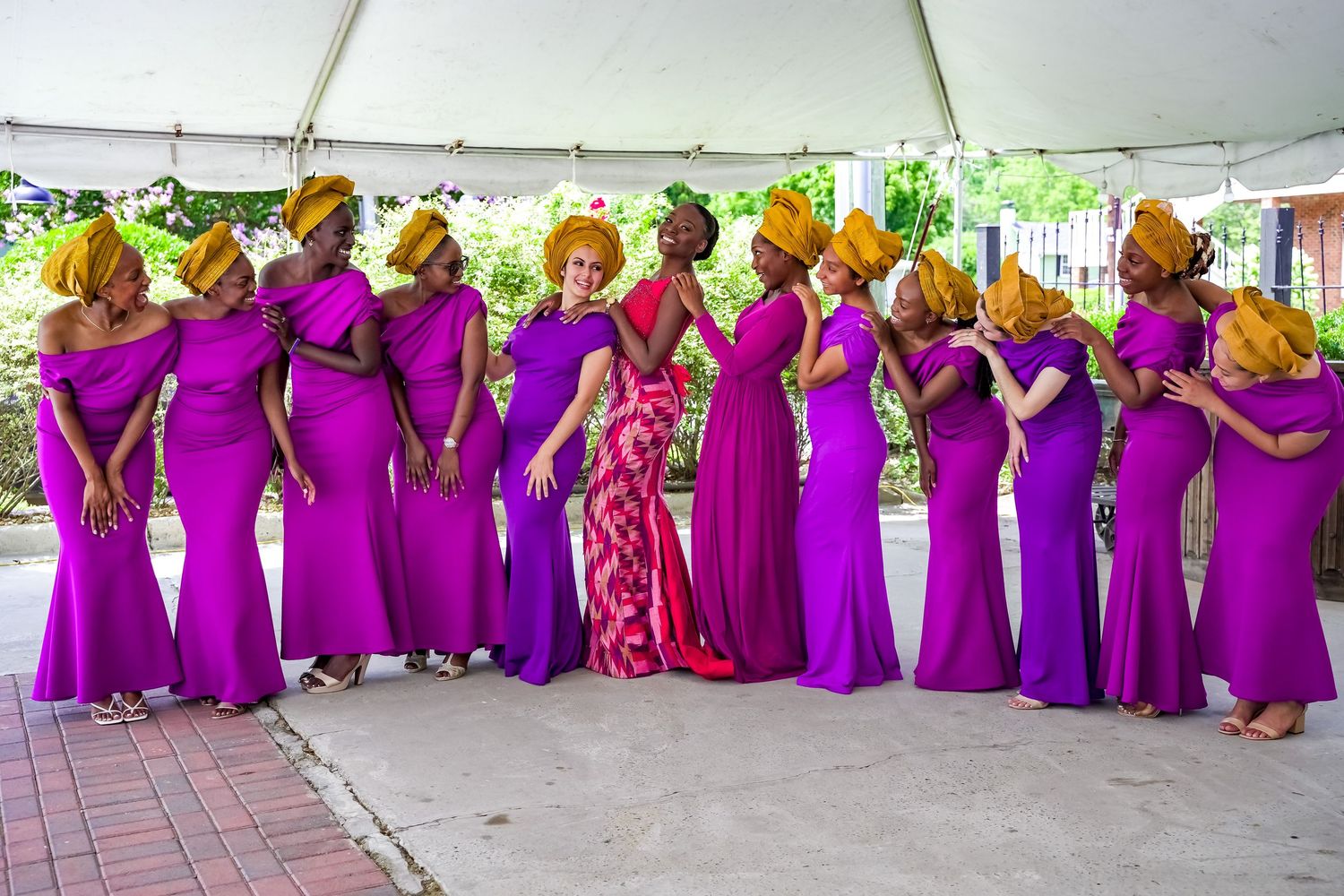 Bridesmaids in purple gowns and gold headwraps pose in a line at outdoor wedding.