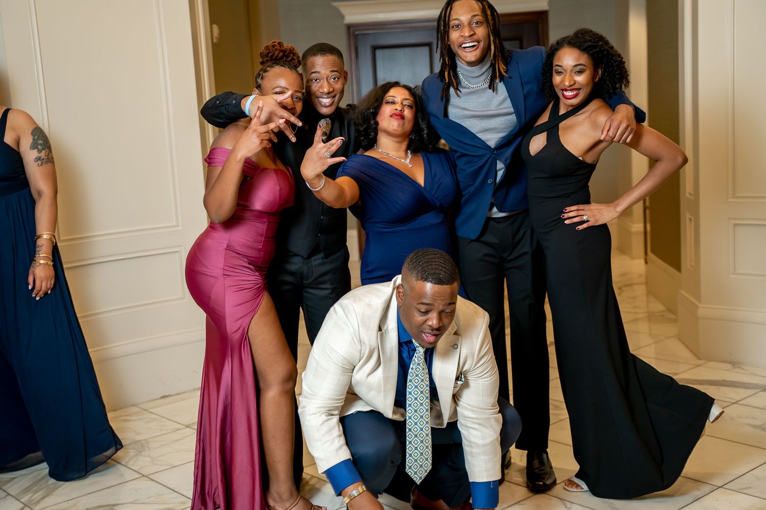 Smiling group dressed in formal attire posing energetically in an elegant event venue hallway.