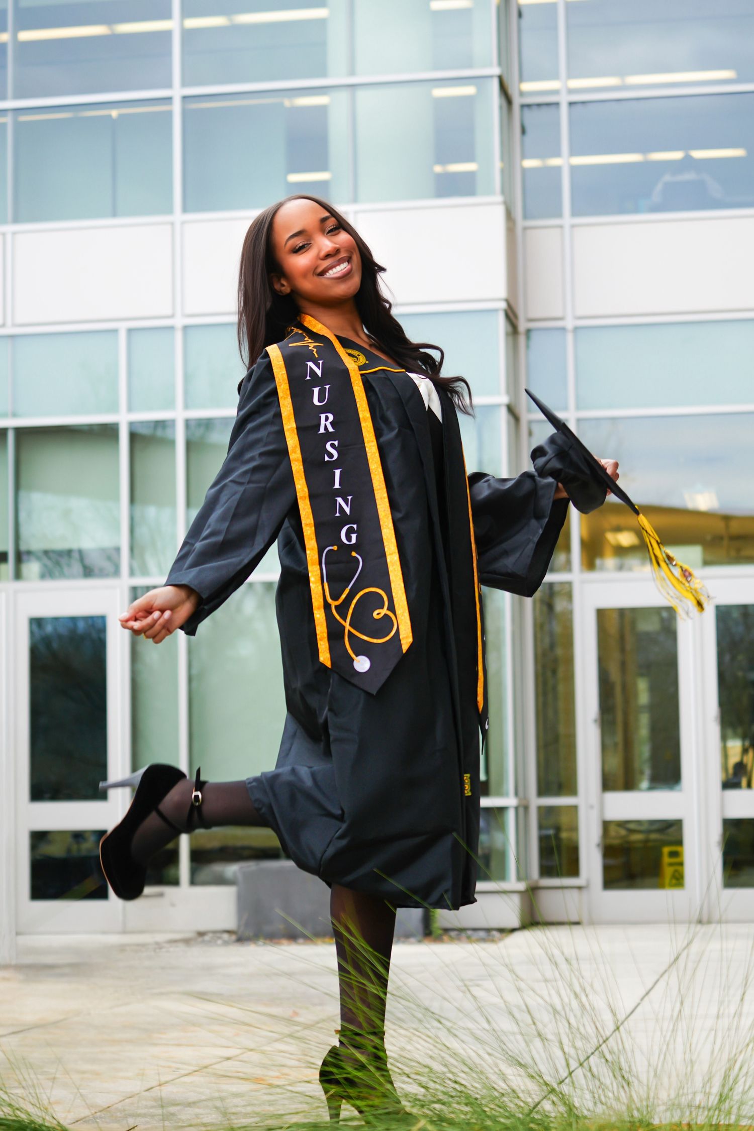 Happy nursing graduate in cap and gown poses outside Kennesaw State University building.