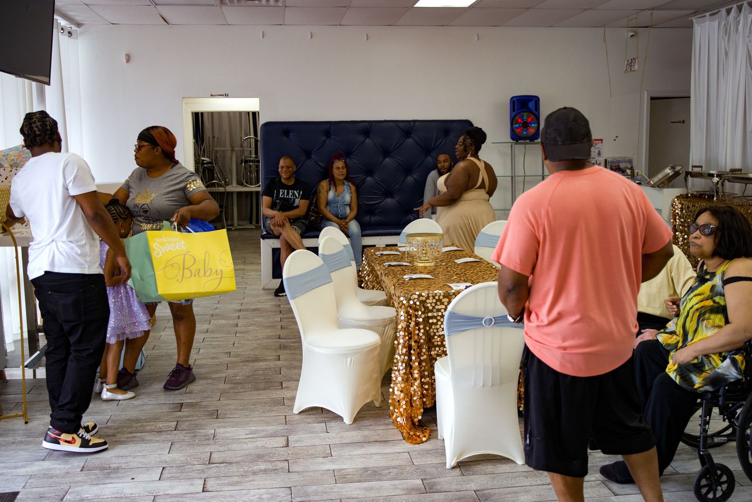 Diverse group of people gathered at an indoor event with gold and white table decorations.