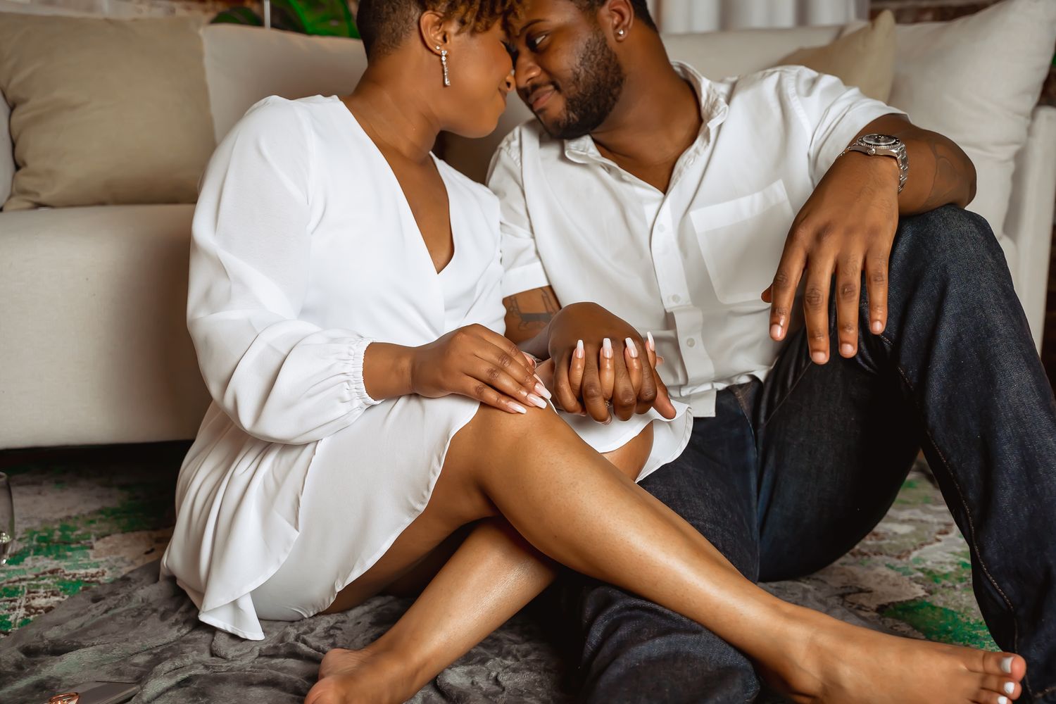 Intimate couple sits together on floor in matching white shirts sharing a quiet romantic moment.