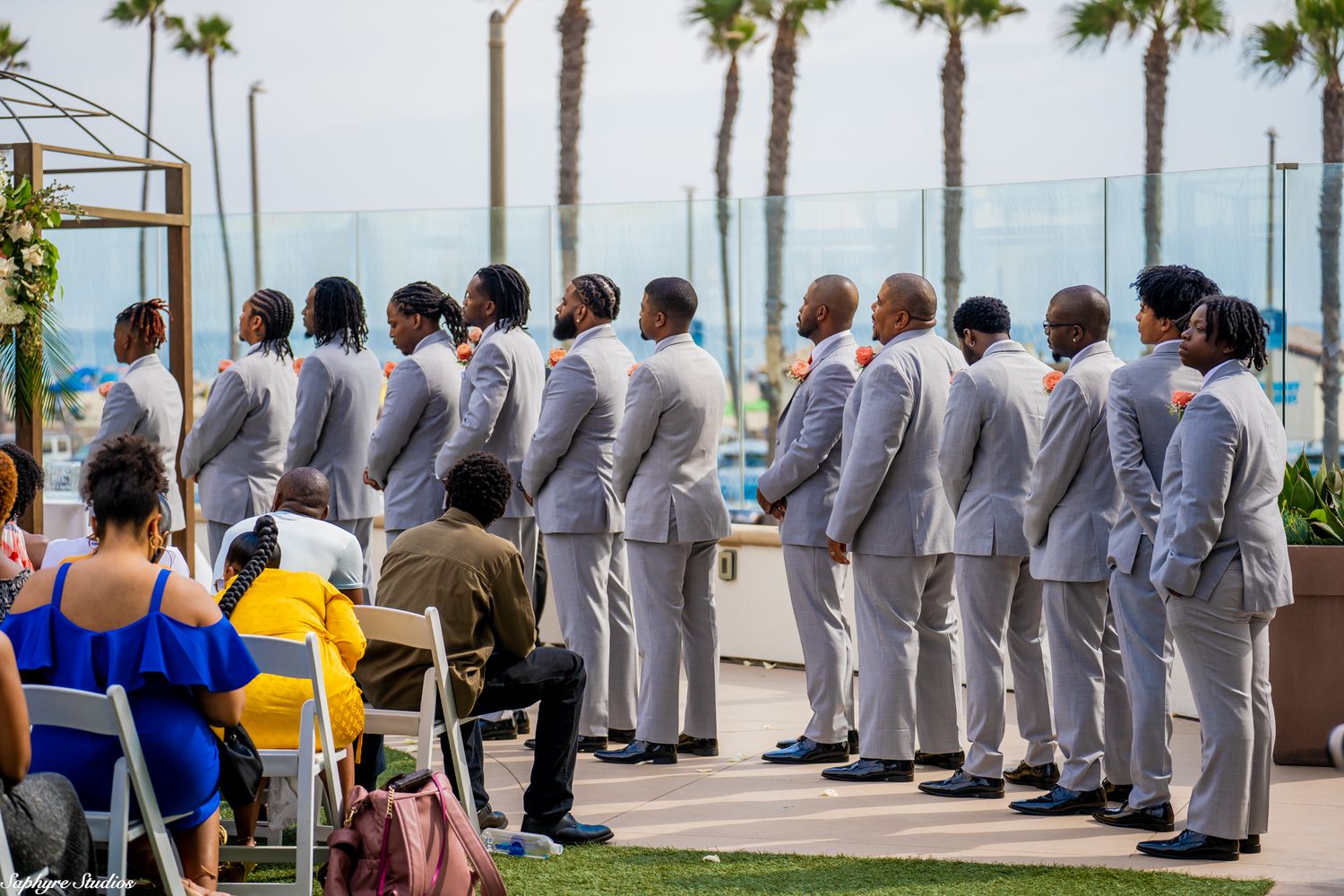 Row of groomsmen in matching gray suits stand at attention during outdoor wedding ceremony.