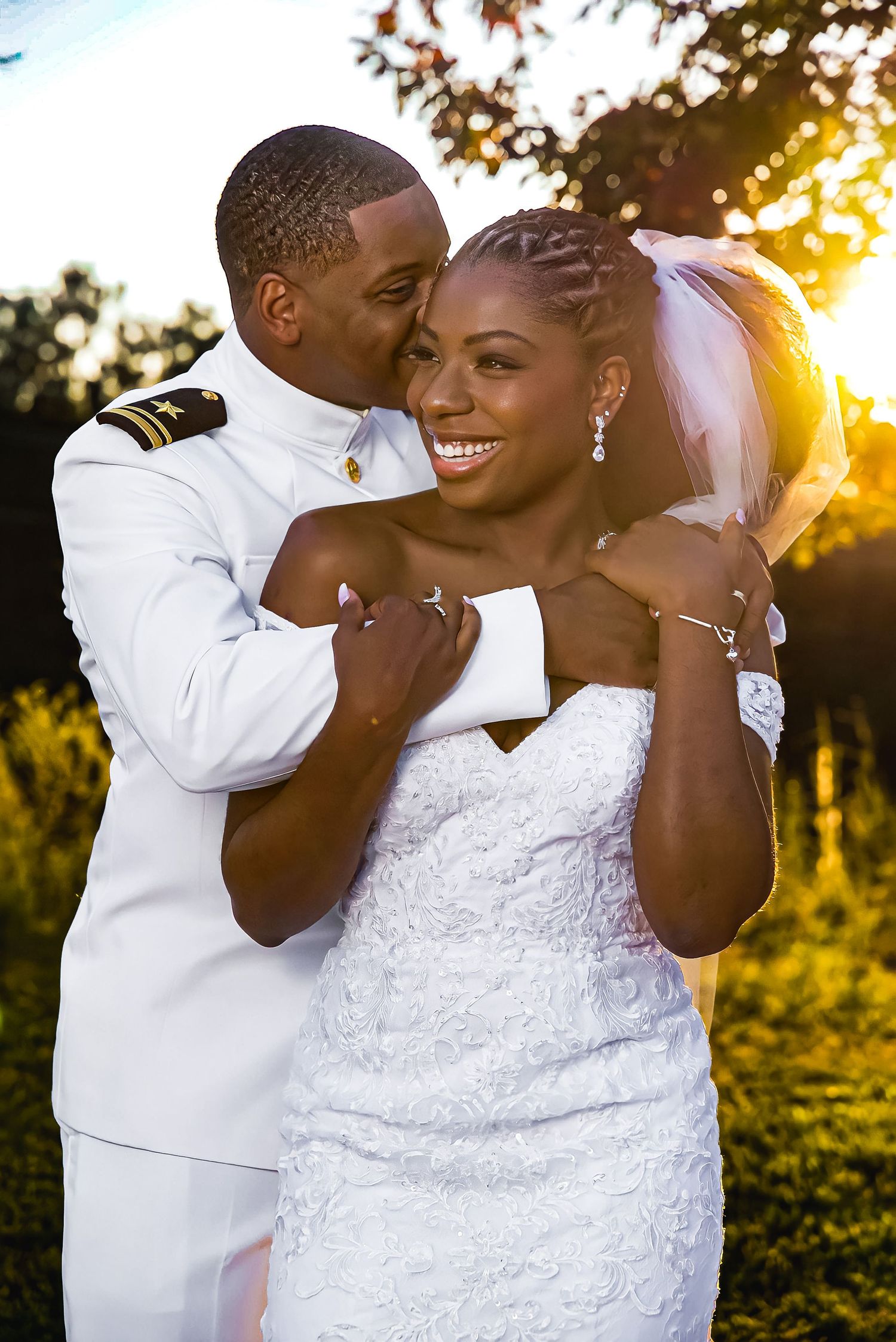 Military groom in white dress uniform embraces smiling bride during golden hour wedding portrait.