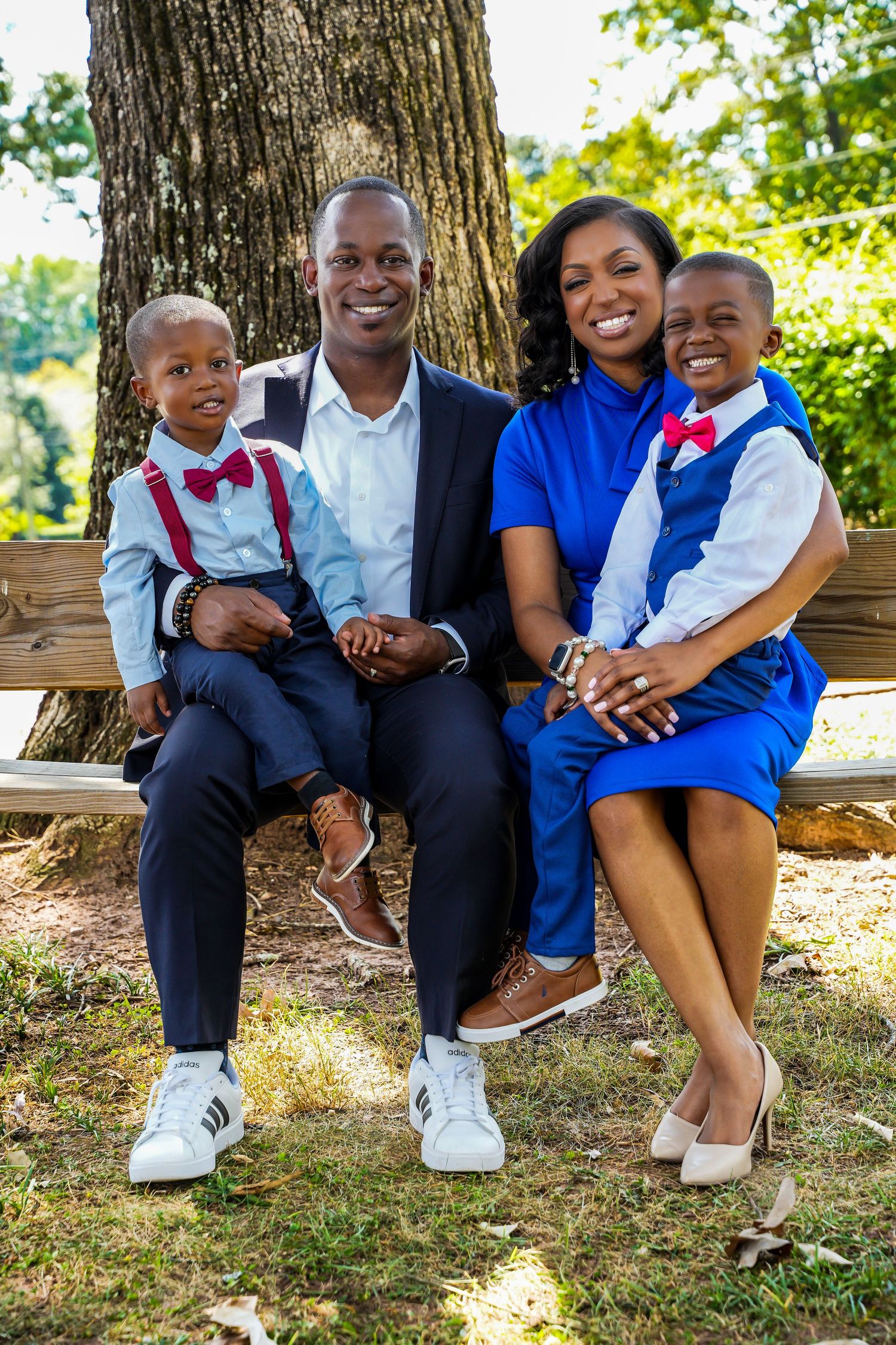 Happy African American family of four posing on a bench outdoors wearing coordinated blue and red outfits.