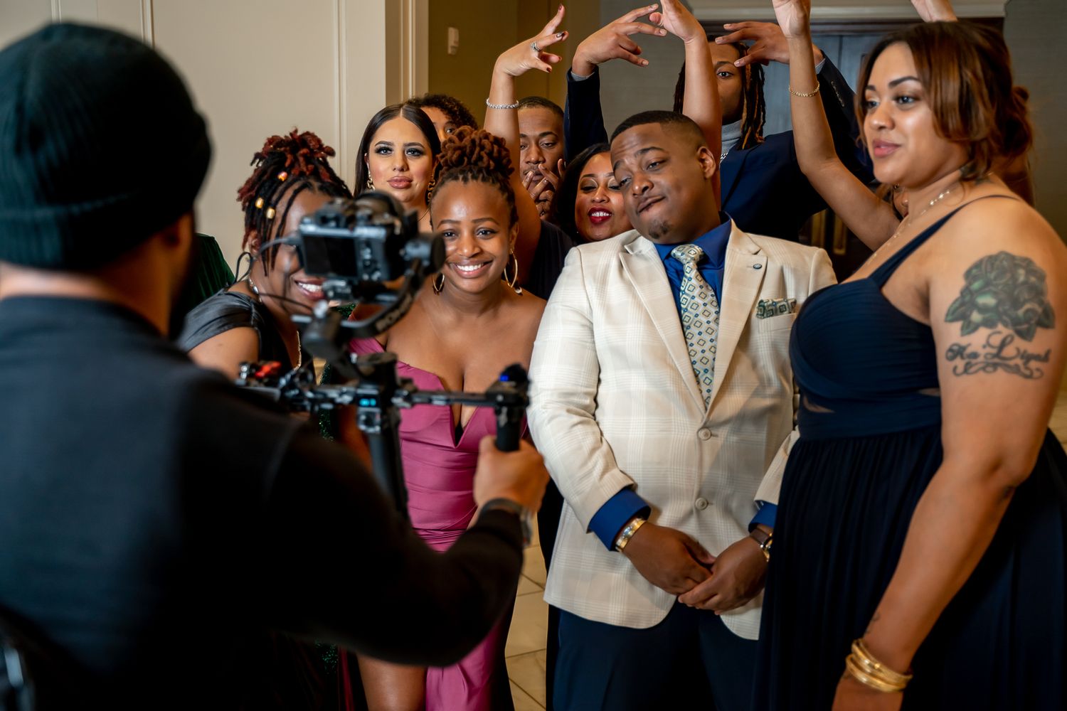 Group of dressed-up friends being filmed by videographer at a lively formal party event.