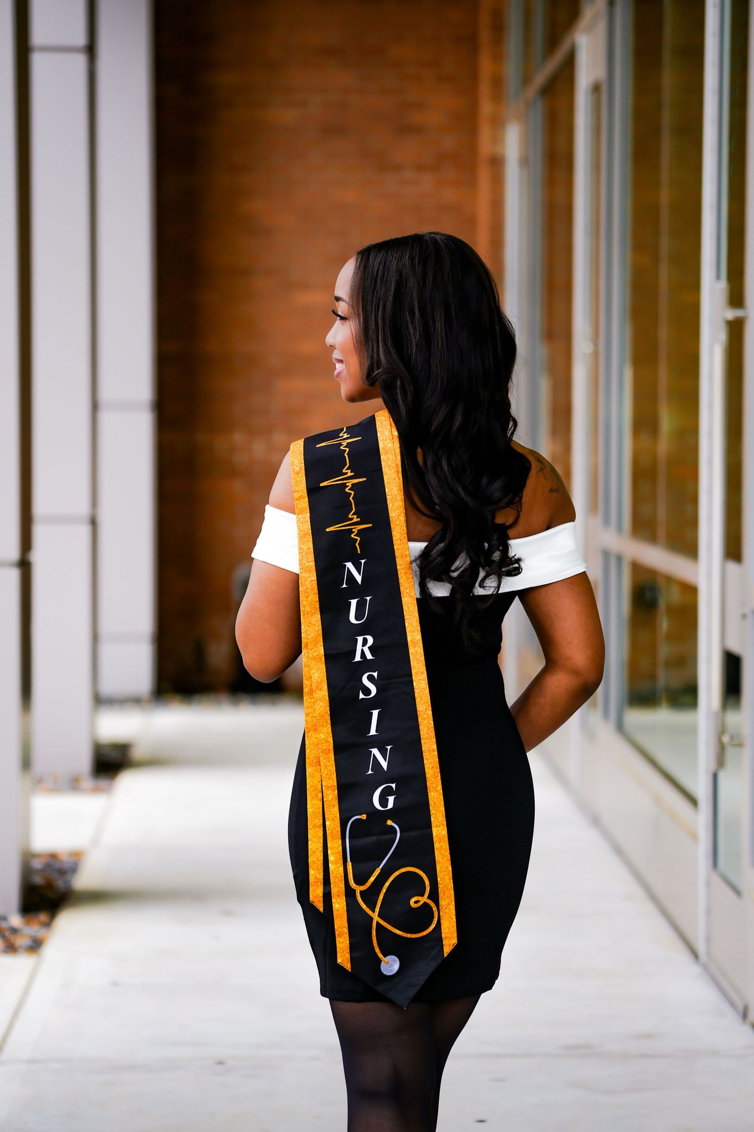 Smiling nursing graduate wearing black and gold NURSING graduation sash poses outdoors at Kennesaw State University.