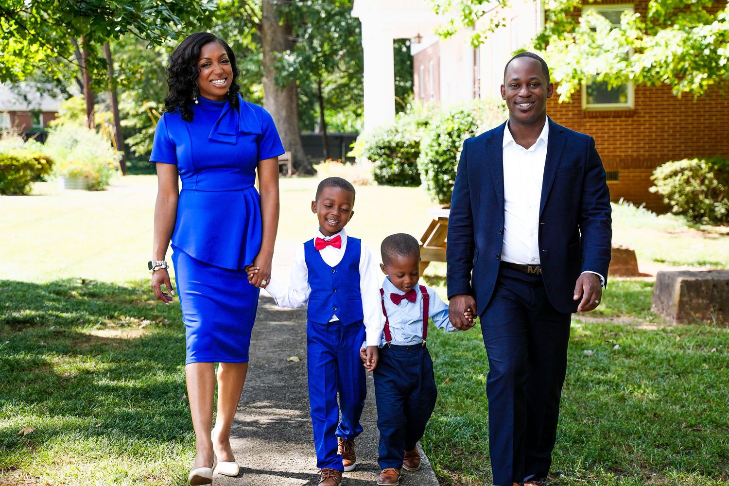 Joyful African American family of four walking hand in hand outdoors in coordinated blue and red attire.