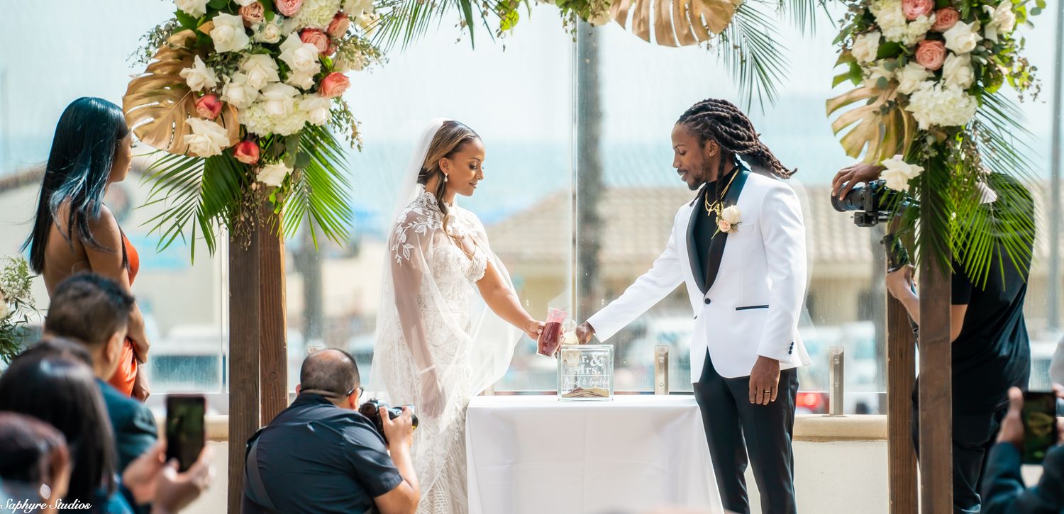 Bride and groom perform unity ceremony at decorated table during outdoor waterfront wedding.