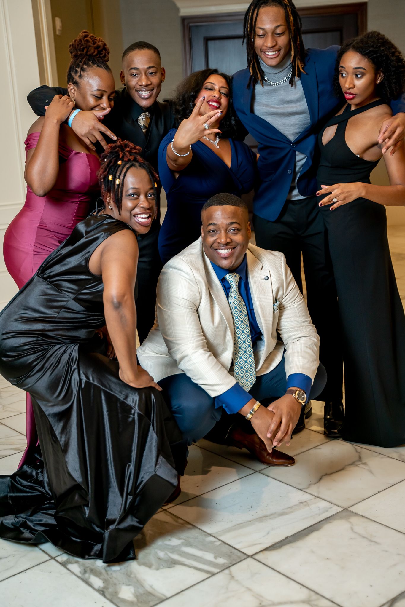 Group of friends in formal attire laughing and posing playfully at a gala.