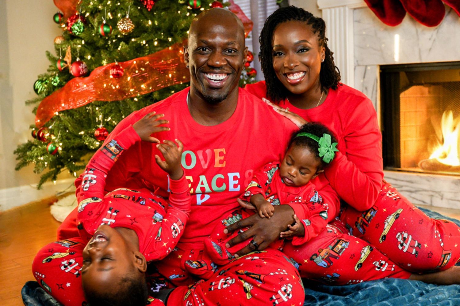 Happy family in matching red Christmas pajamas posing together near decorated holiday tree.