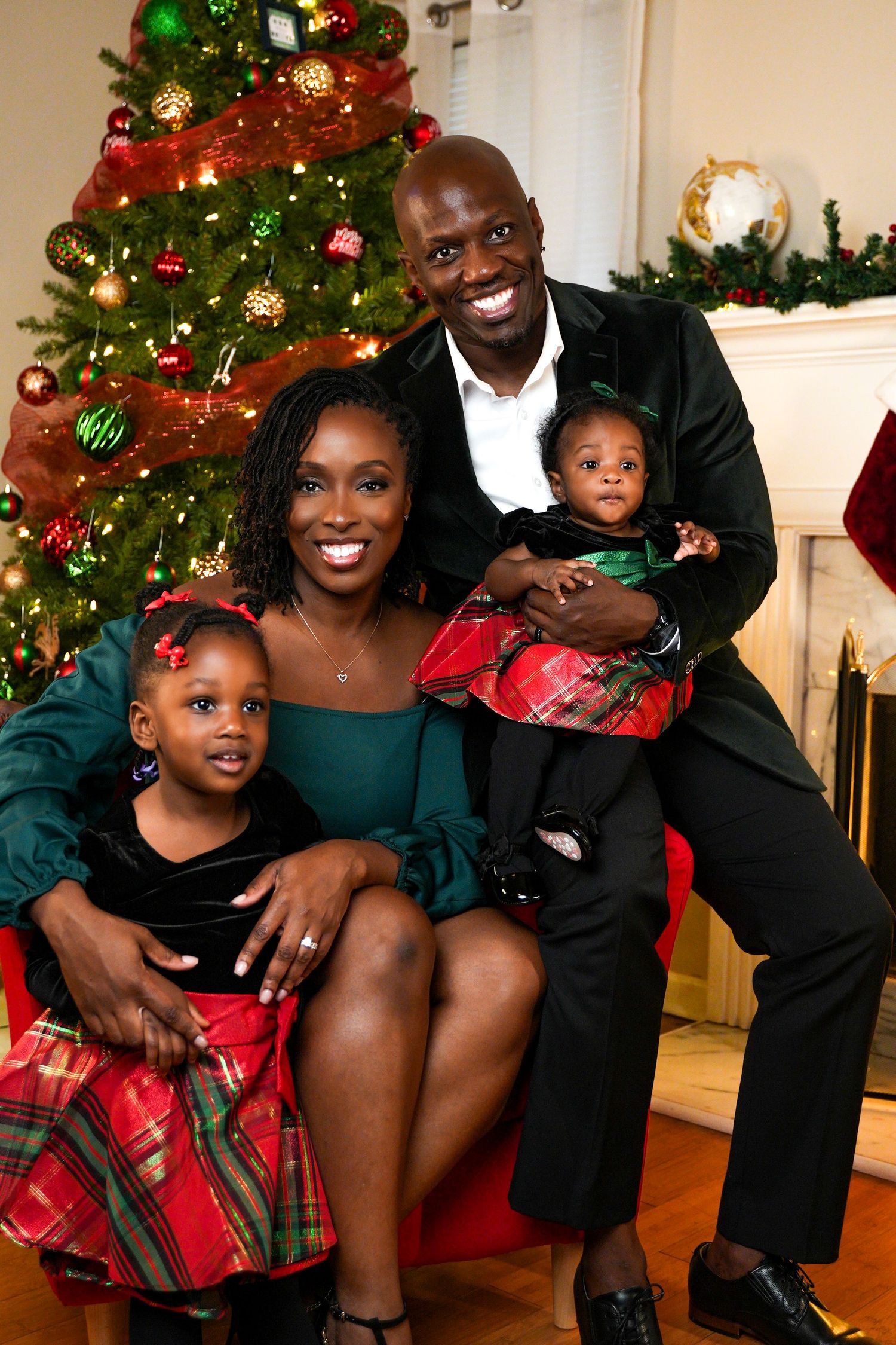 Smiling family of four in festive holiday attire posing in front of a decorated Christmas tree.