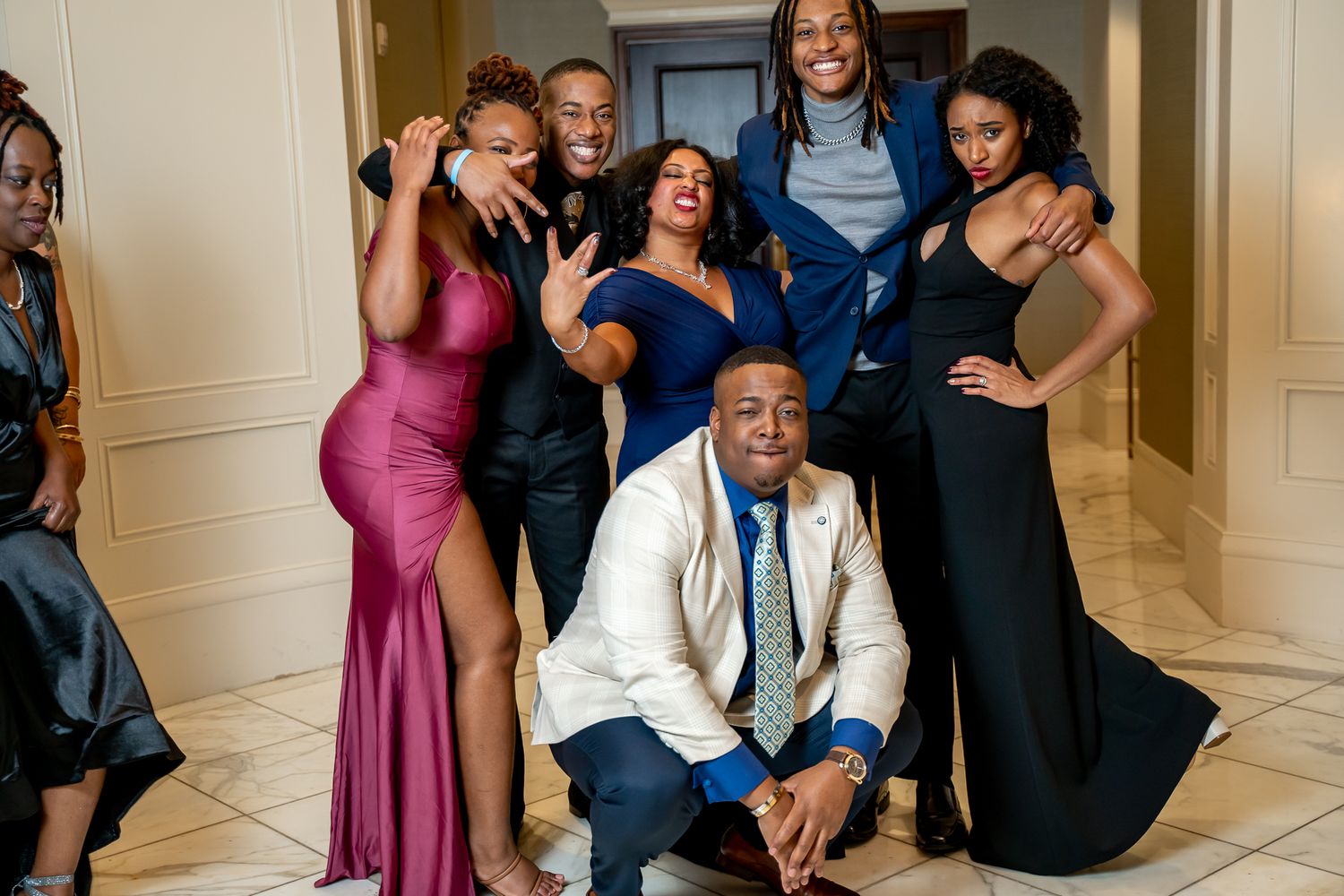 Cheerful group in elegant formal attire posing together in a bright carpeted event hallway.