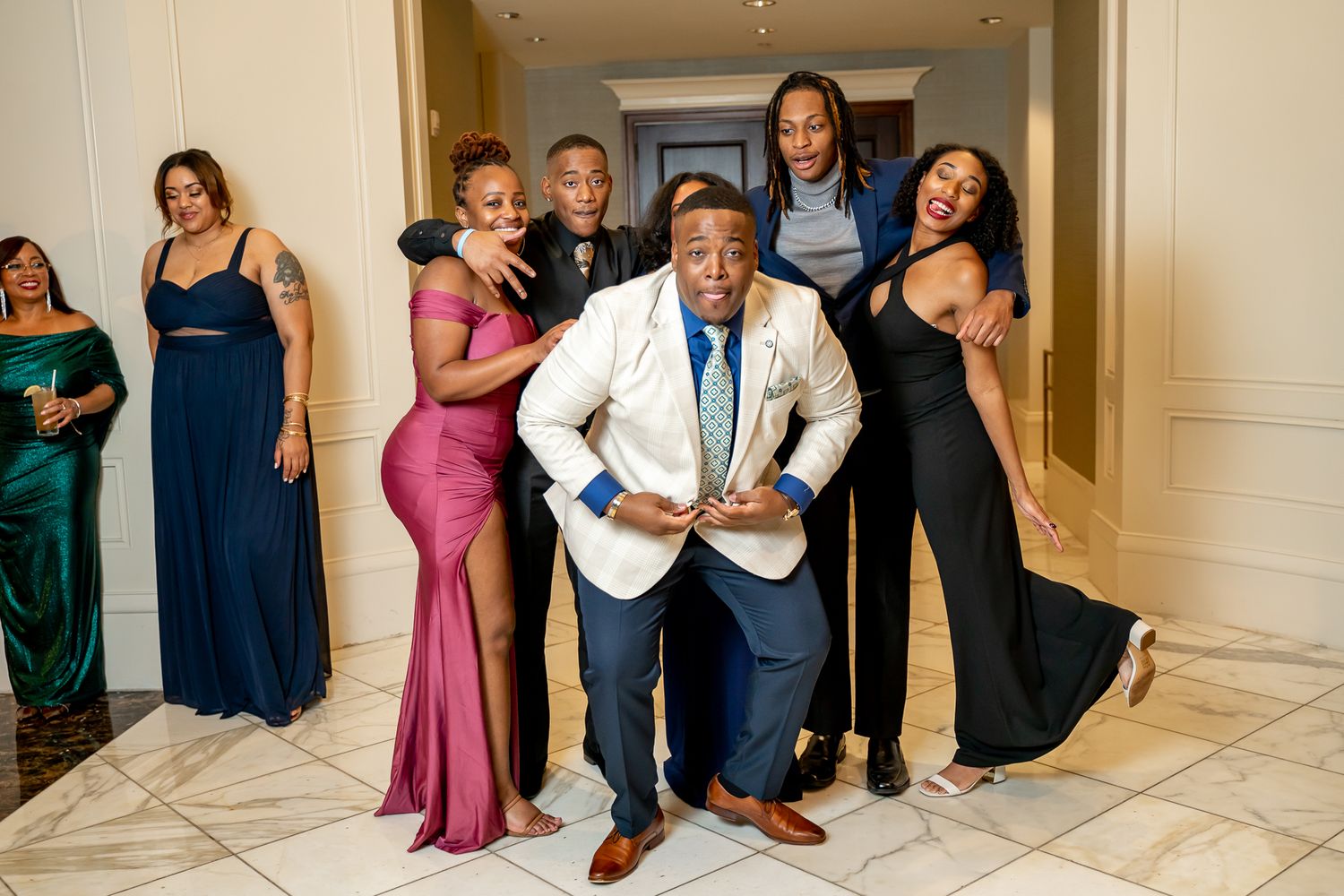 Joyful group in formal wear striking fun poses in an elegant hallway at a formal event.