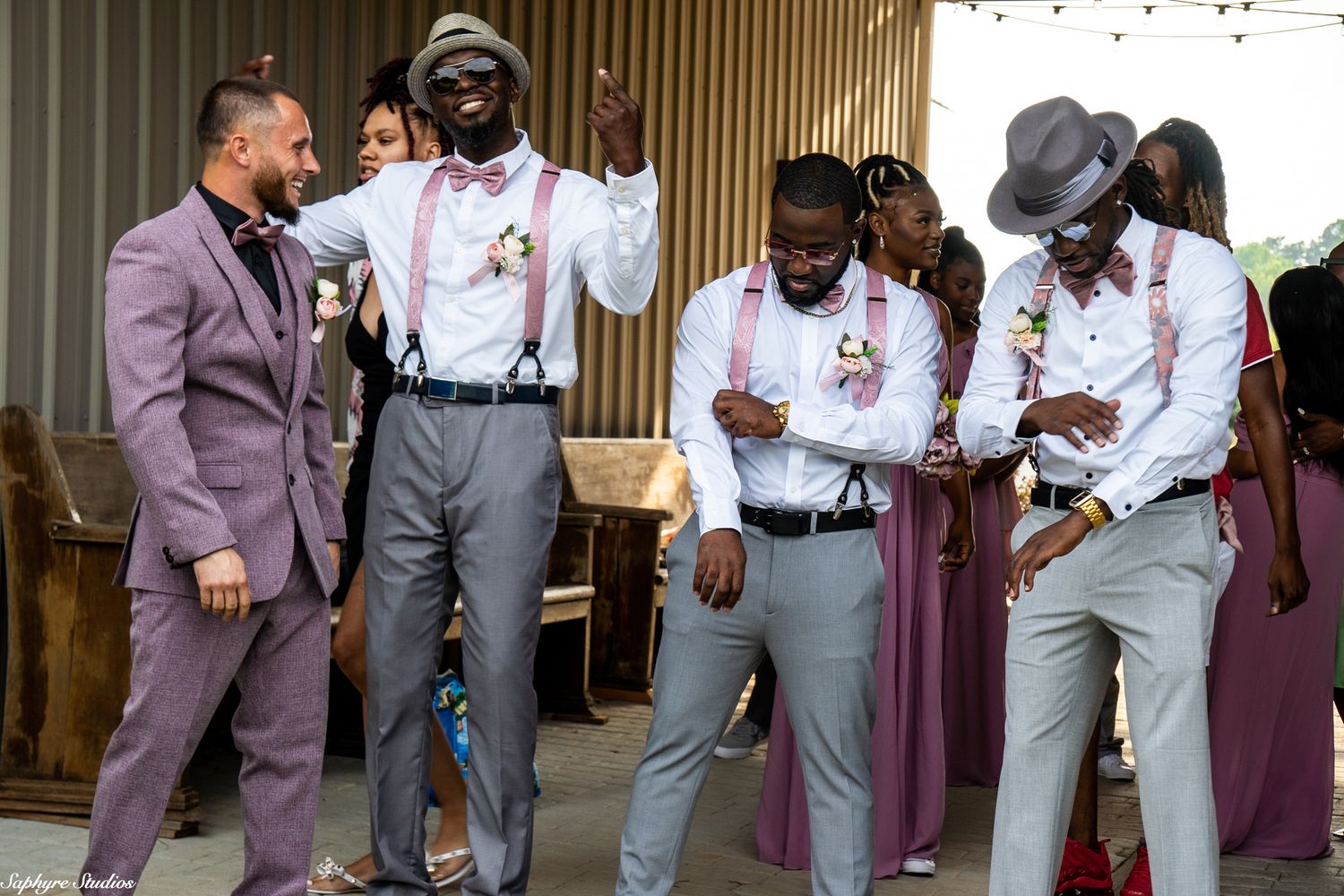 Groom and groomsmen in pink suspenders dancing and celebrating before the outdoor wedding ceremony.