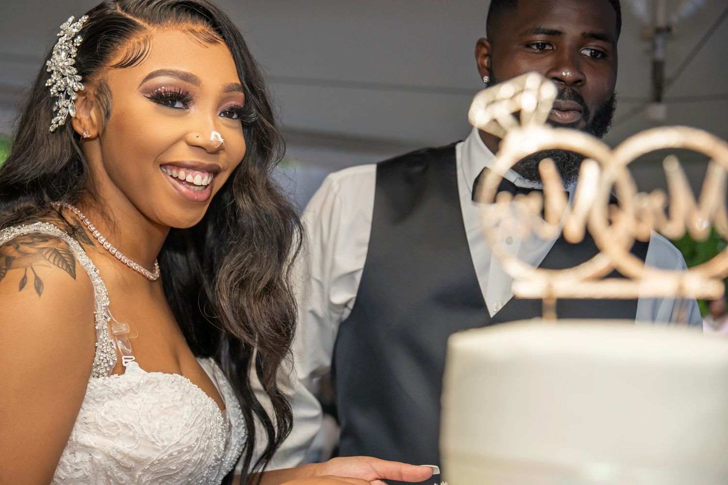 Bride and groom smile while cutting elegant white wedding cake with monogram topper.