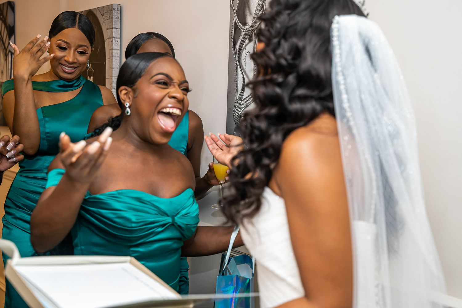 Excited bridesmaid in teal dress reacting with joy upon seeing bride in white gown and veil.