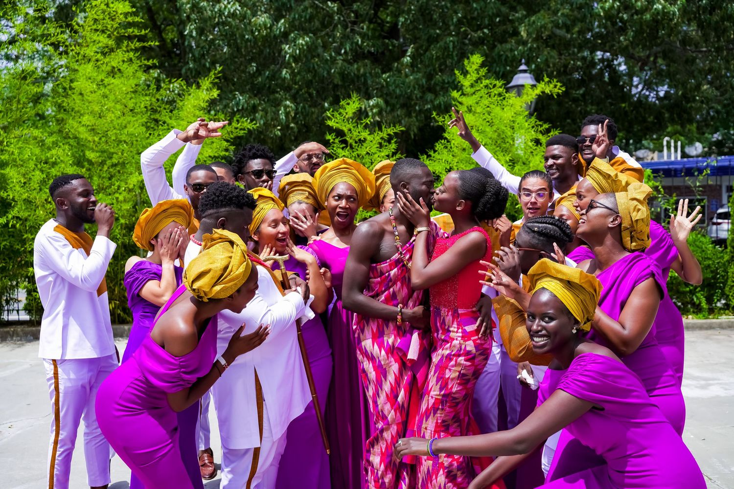 A joyful group celebrating in vibrant purple and gold African attire outdoors.
