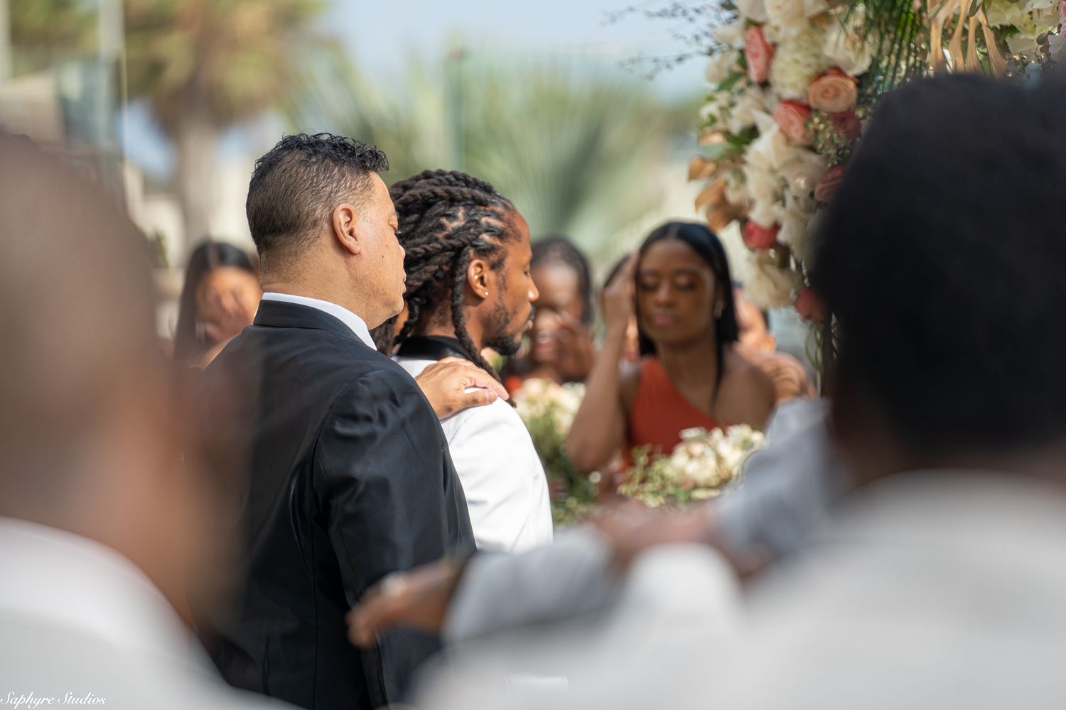 Groom receives congratulatory hug from guest following outdoor wedding ceremony.