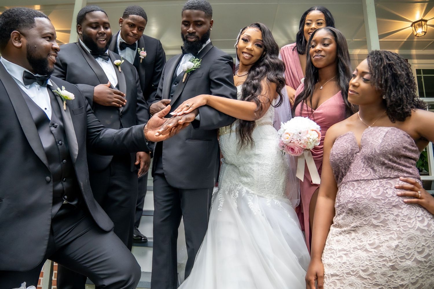 Bride and groom share a joyful moment with wedding party on elegant staircase.