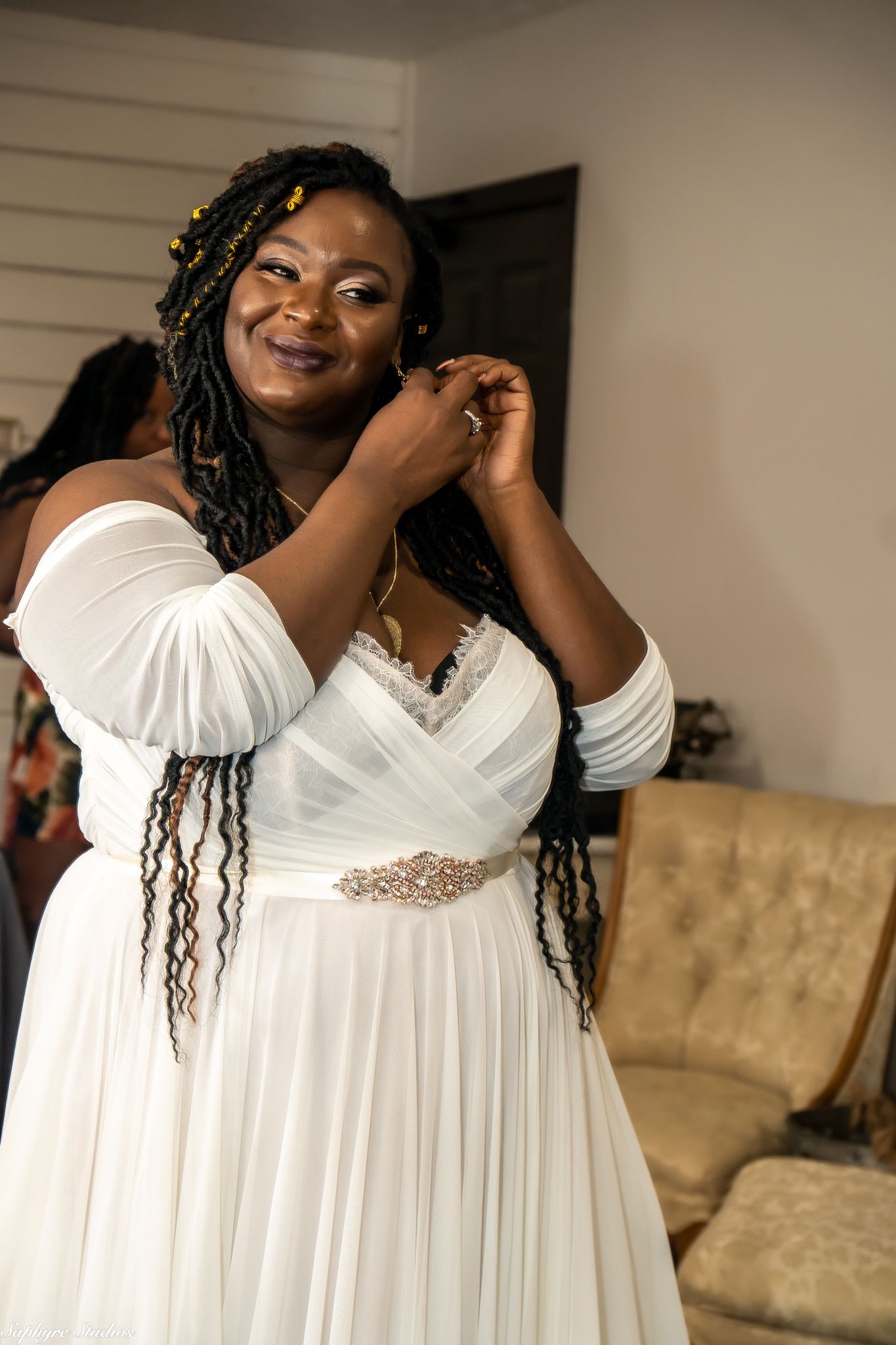 Beautiful bride in off-shoulder white wedding gown adjusting her earrings before the ceremony.