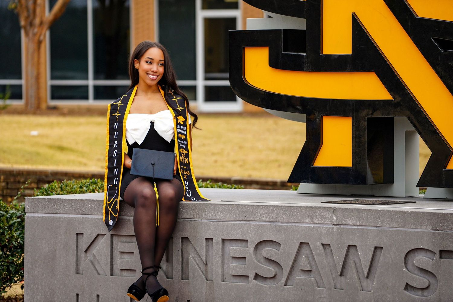 Graduate posing at Kennesaw State University sign in black and gold regalia.