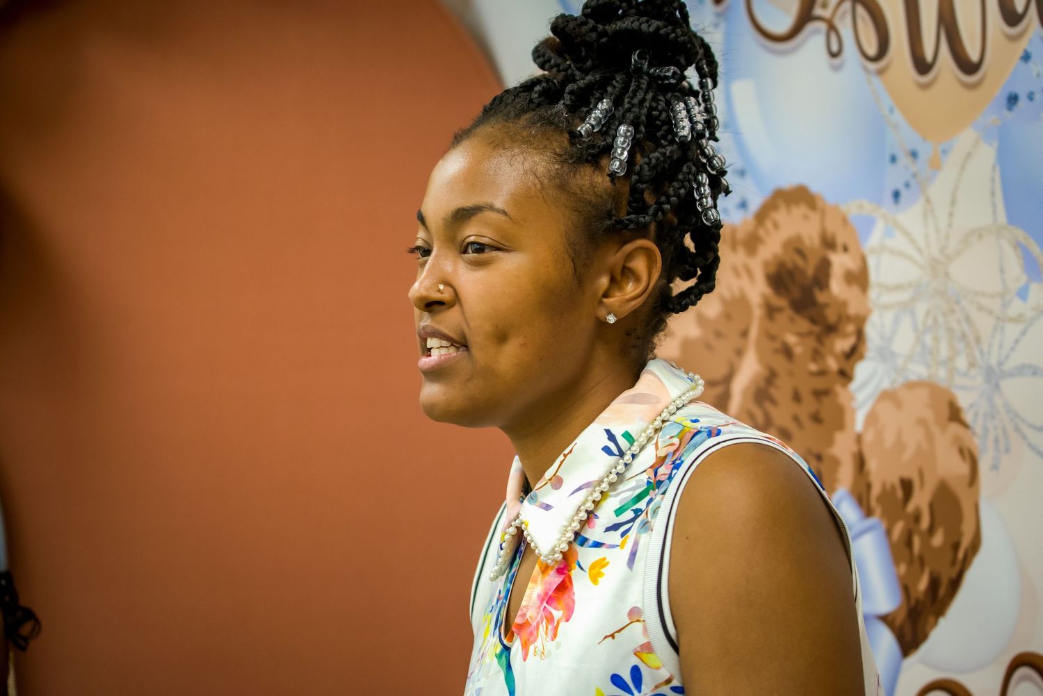 Woman with natural hair speaking at event in front of decorative banner backdrop.