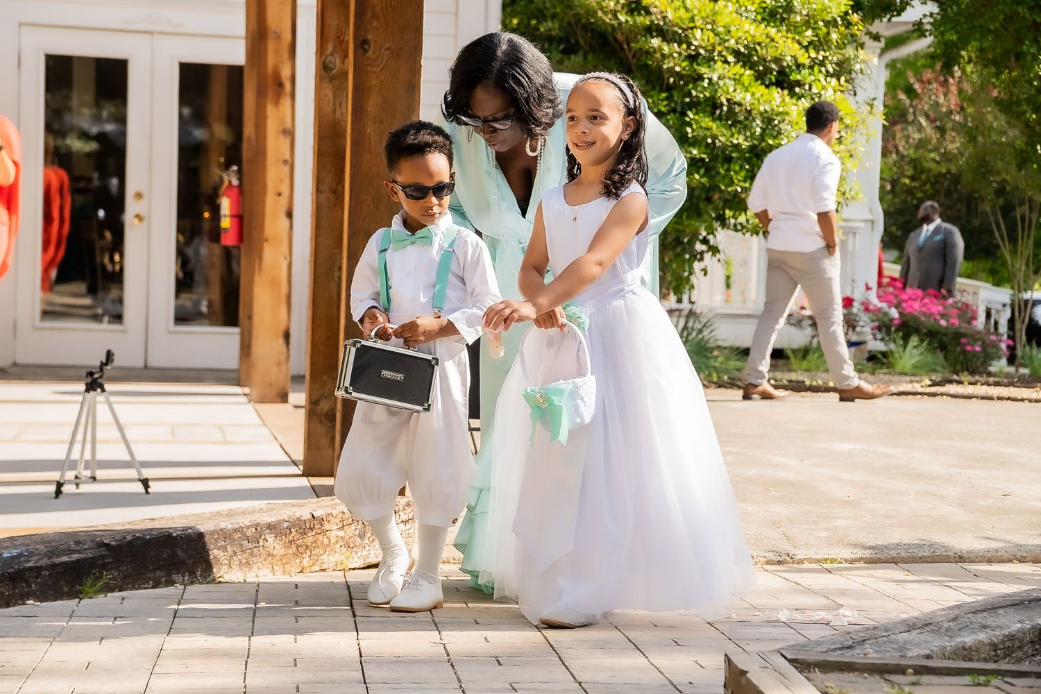 A woman in white helps two children in wedding attire on an outdoor patio.