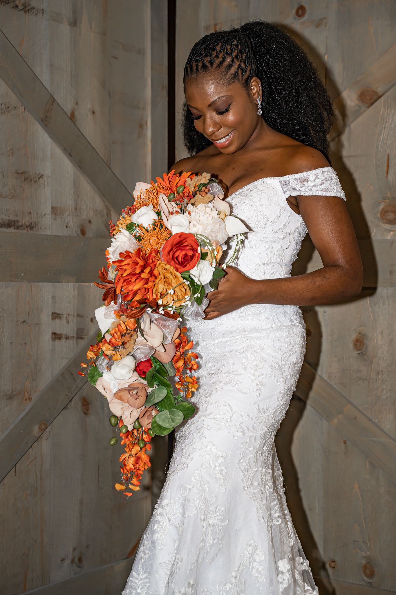 Beautiful Black bride in off-shoulder lace mermaid gown holding cascading orange and white floral bouquet.