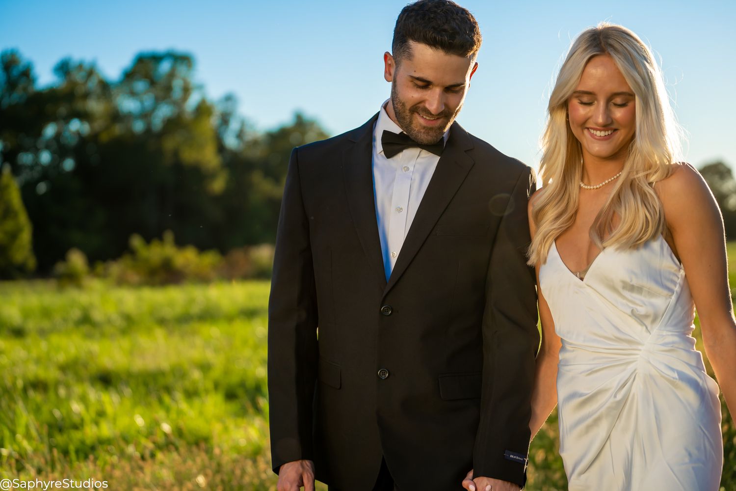 Smiling bride and groom sharing a tender moment together on a sunny green field.