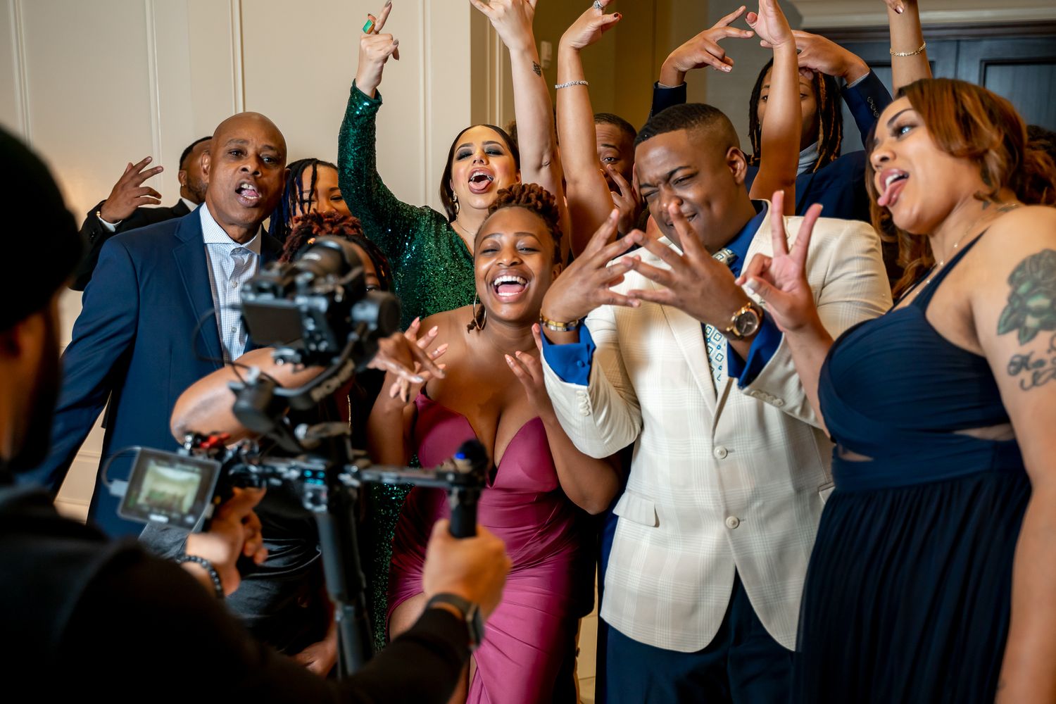 Lively group of elegantly dressed friends laughing and celebrating together in front of a video camera.