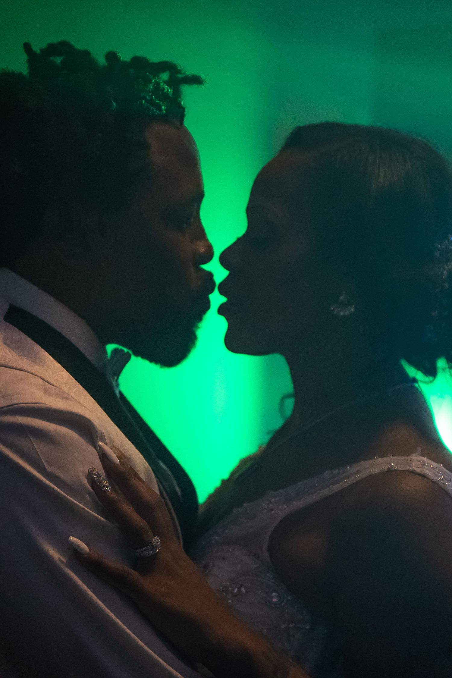 Bride and groom sharing a romantic kiss on the dance floor bathed in green light.