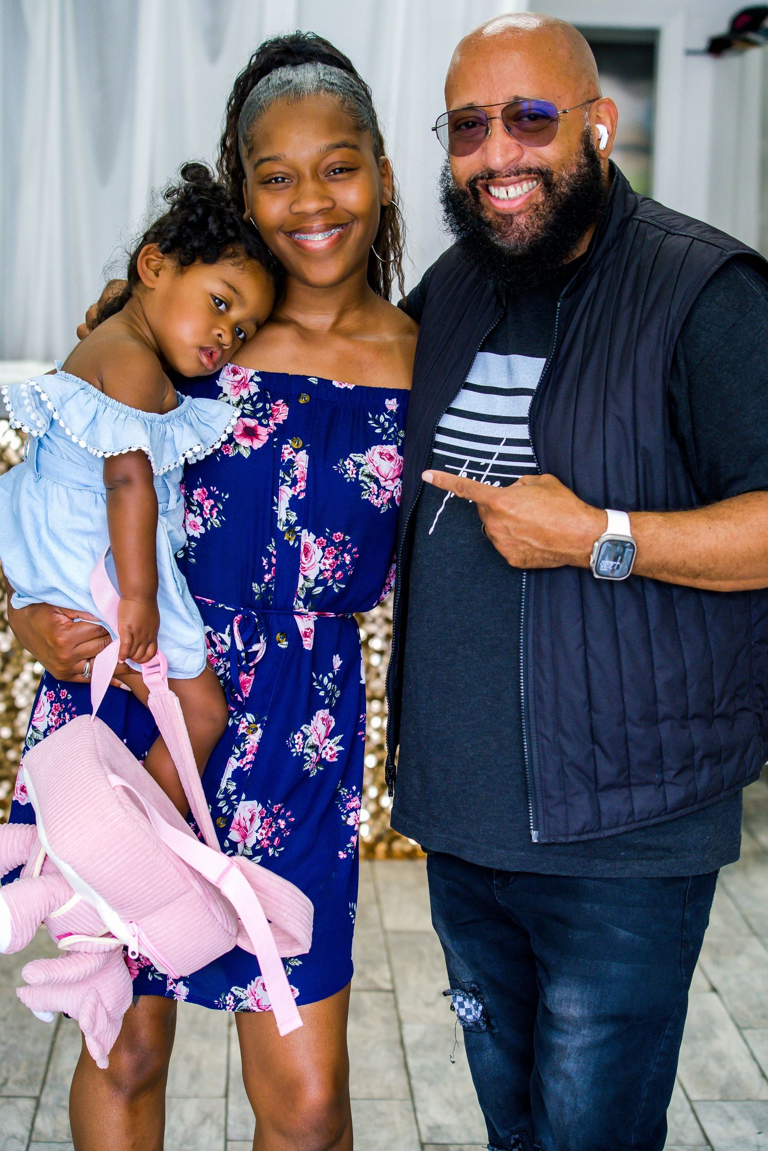 Smiling family of three with young girl in blue dress at a cheerful indoor celebration event.