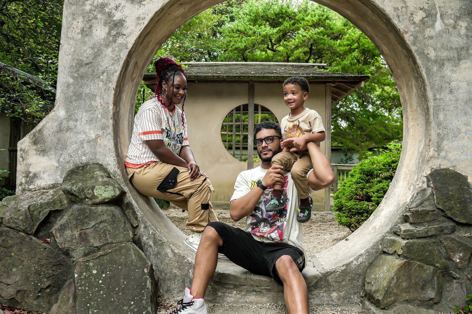 Family enjoying ice cream while posing in a decorative circular stone gate in a green garden setting.