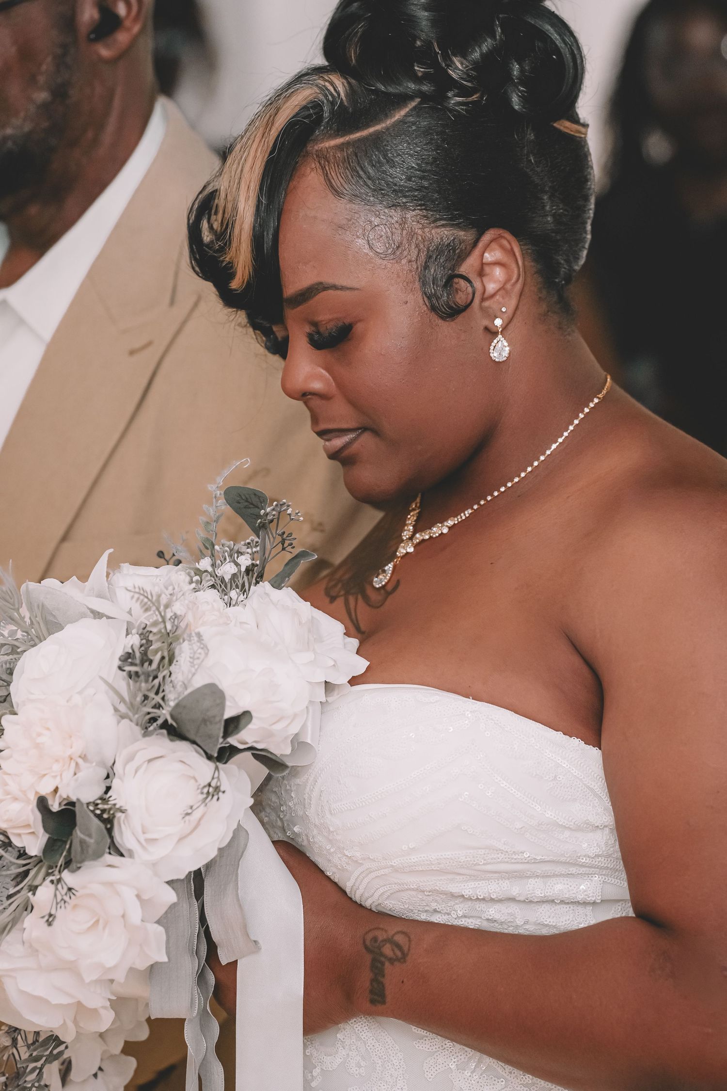Bride in white strapless gown holds white and silver bouquet, wearing pearl jewelry and elegant updo hairstyle.