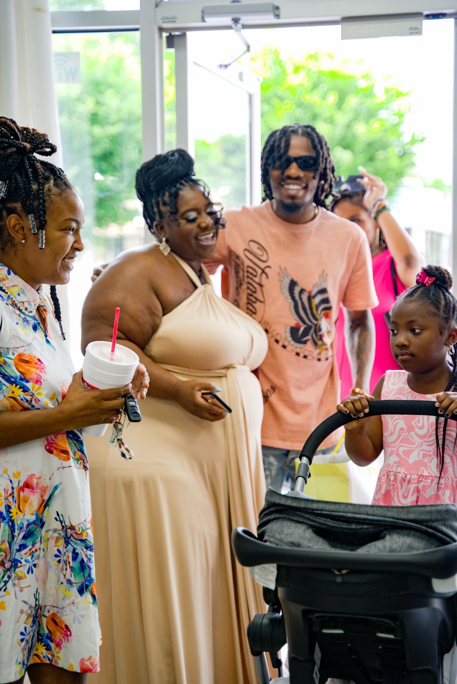 Pregnant woman in beige dress with friends and child admiring baby stroller at shower.