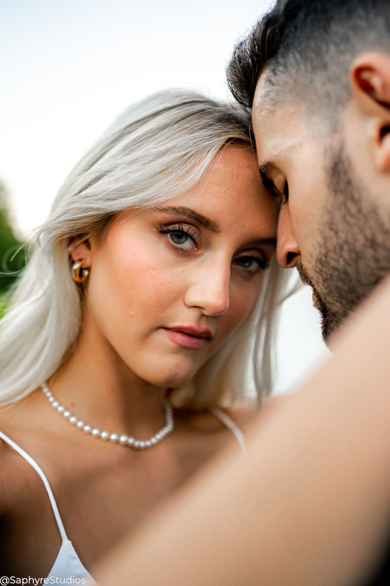 Close-up intimate wedding portrait of blonde bride and bearded groom touching foreheads tenderly.