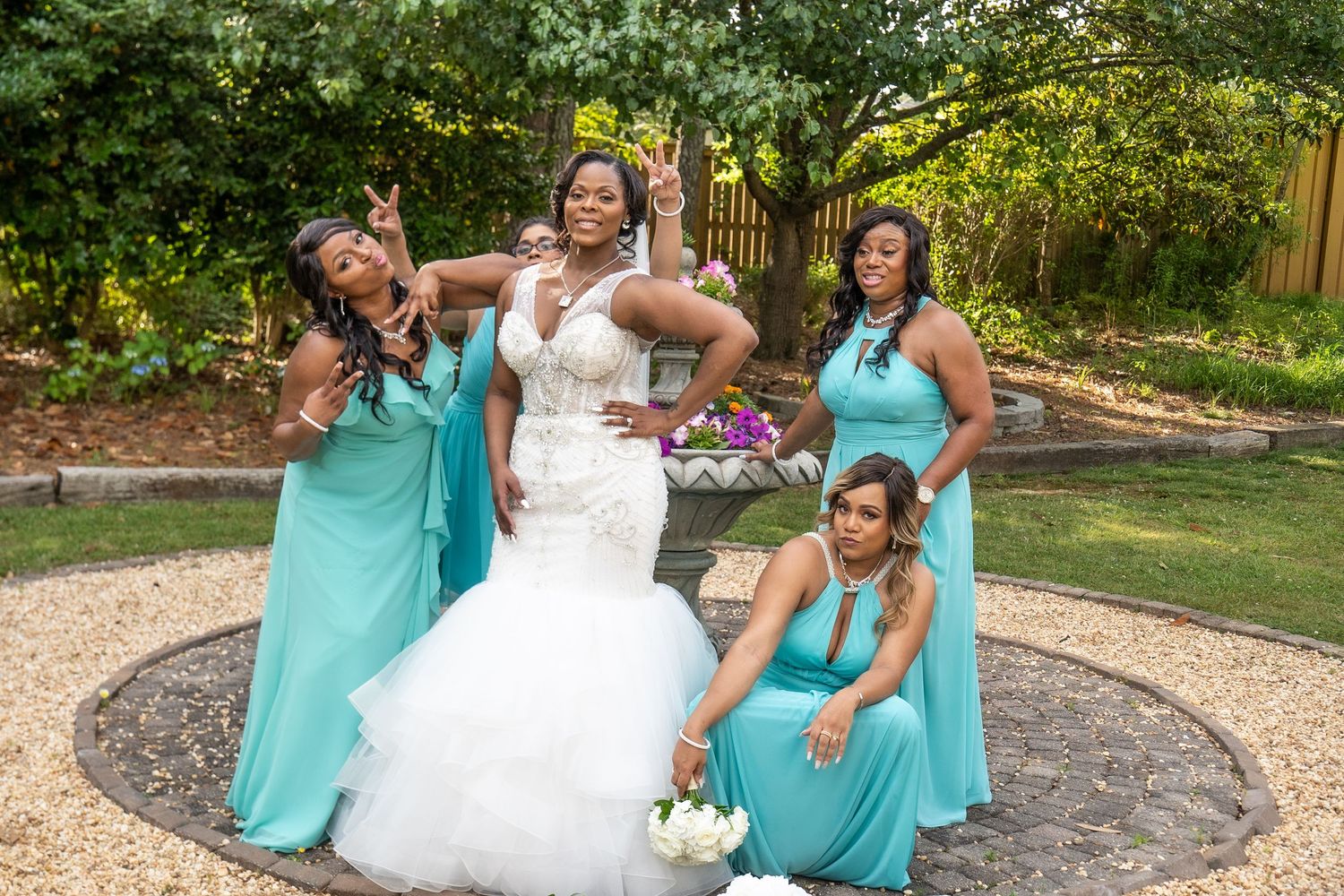 Bride in white mermaid gown poses with three bridesmaids in teal dresses outdoors.