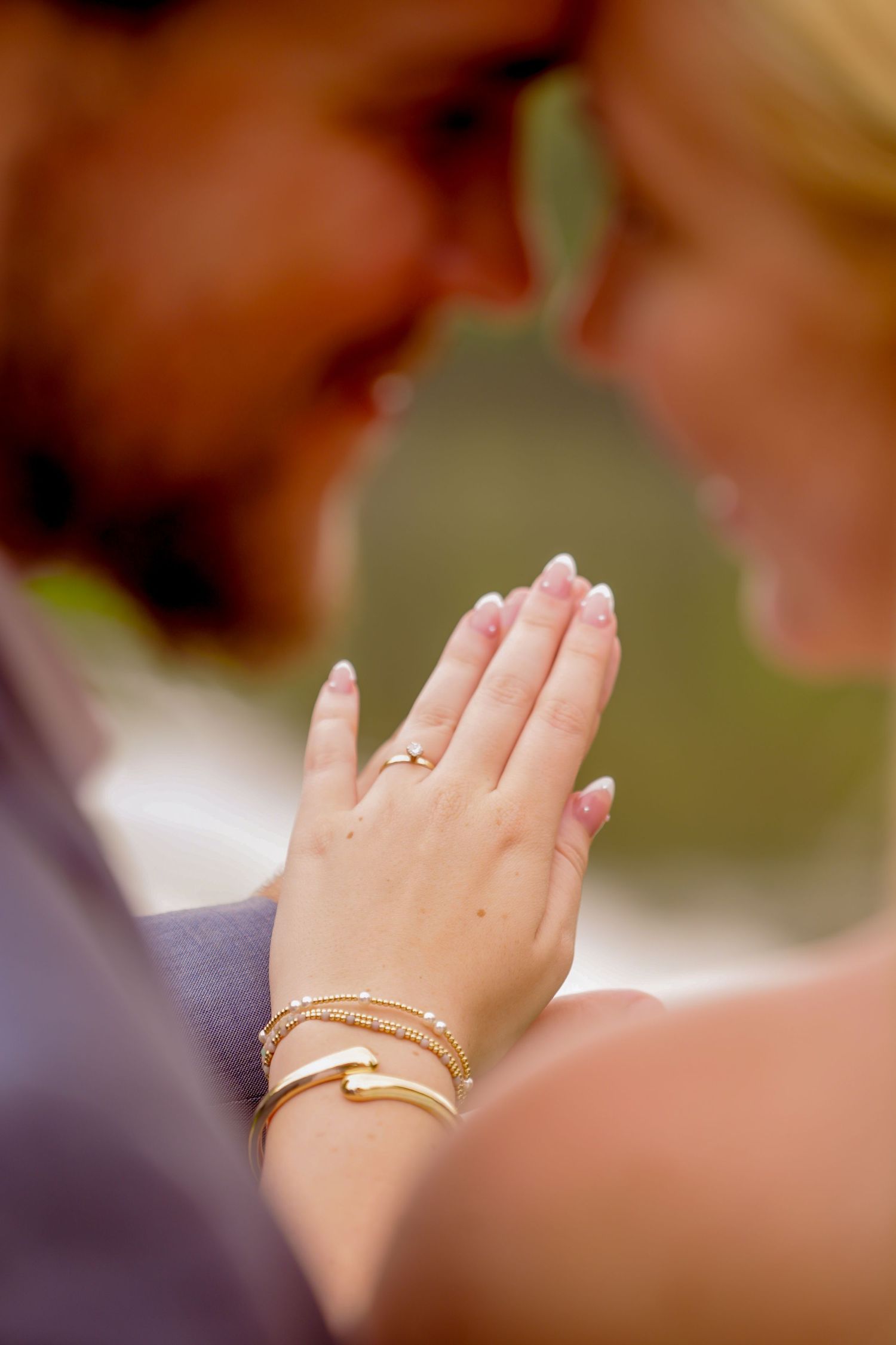 Close-up of a woman's hand with an engagement ring and gold bracelets resting on a man's chest as they embrace.