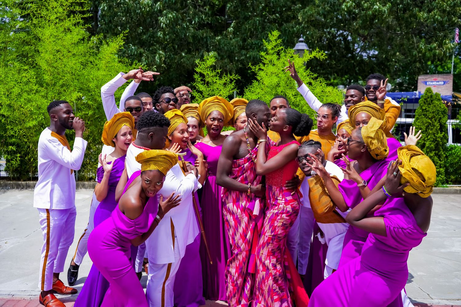 Lively African wedding celebration with guests in purple attire and gold gele dancing outdoors.
