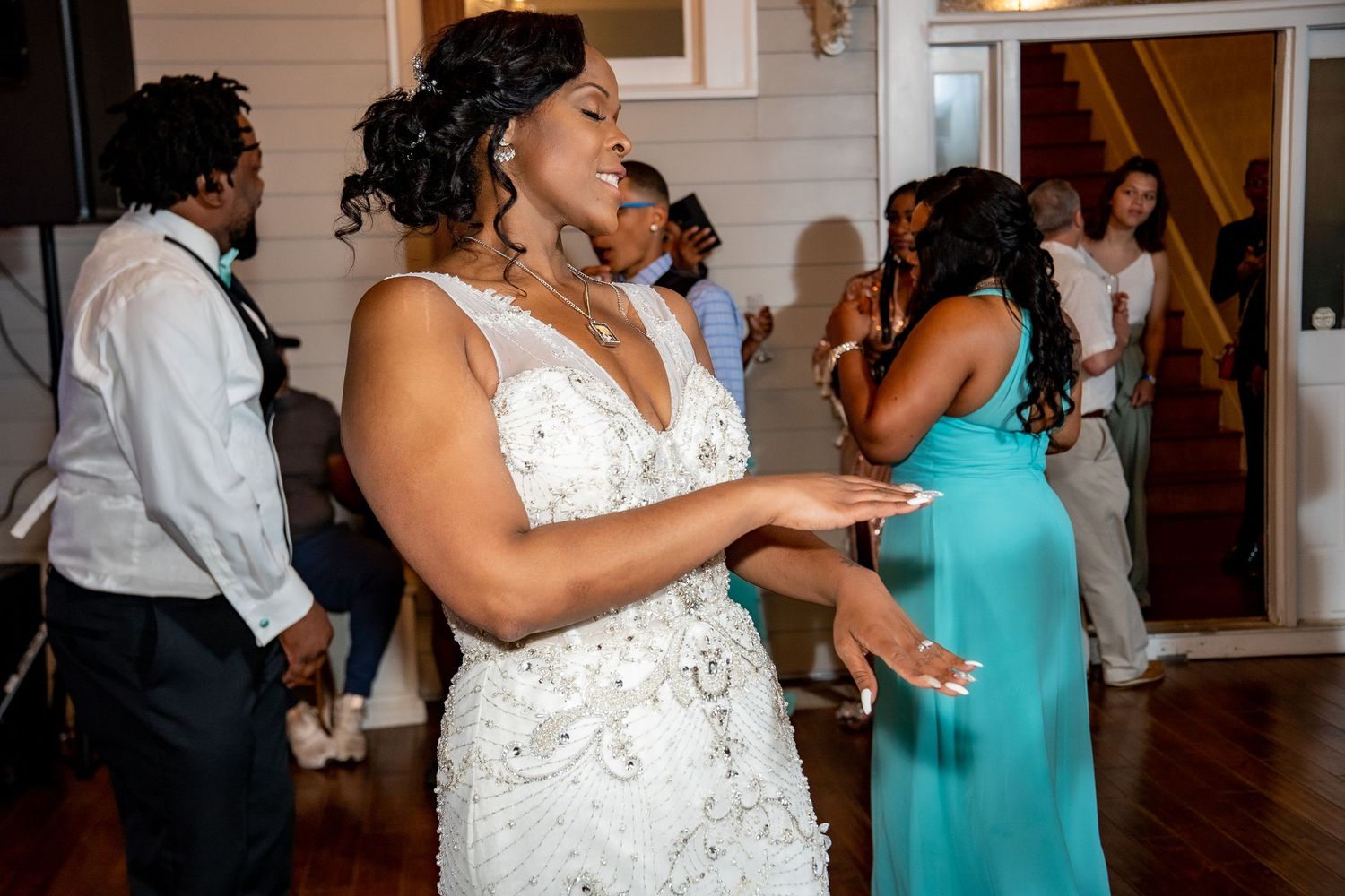 Bride in beaded white gown dances joyfully at wedding reception celebration.