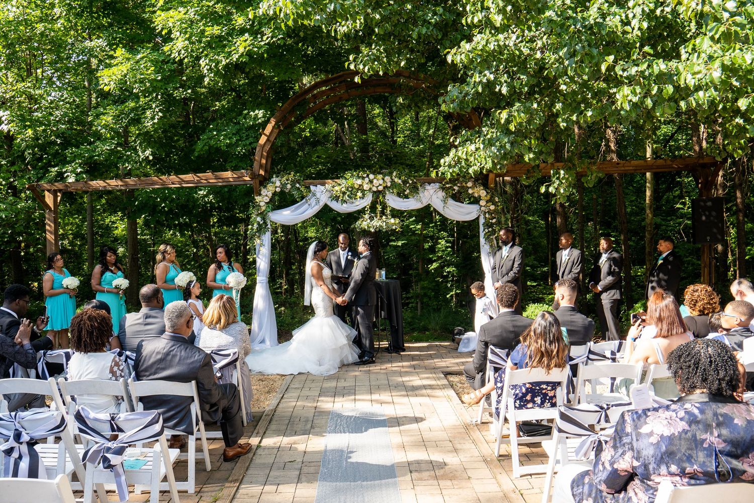 A couple kisses at the altar during an outdoor woodland wedding ceremony with seated guests.