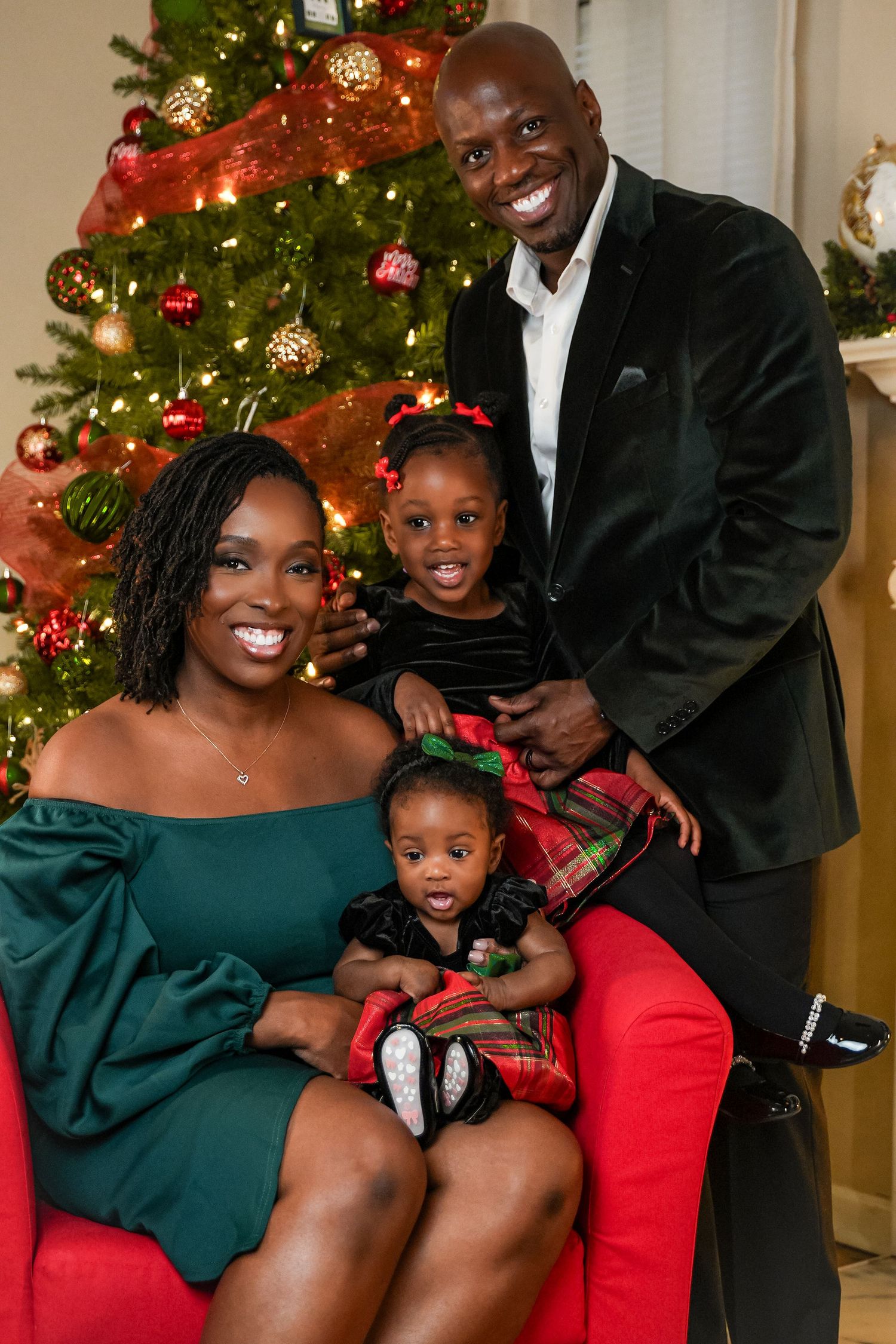 Smiling family of four dressed in holiday outfits poses together in front of a decorated Christmas tree.