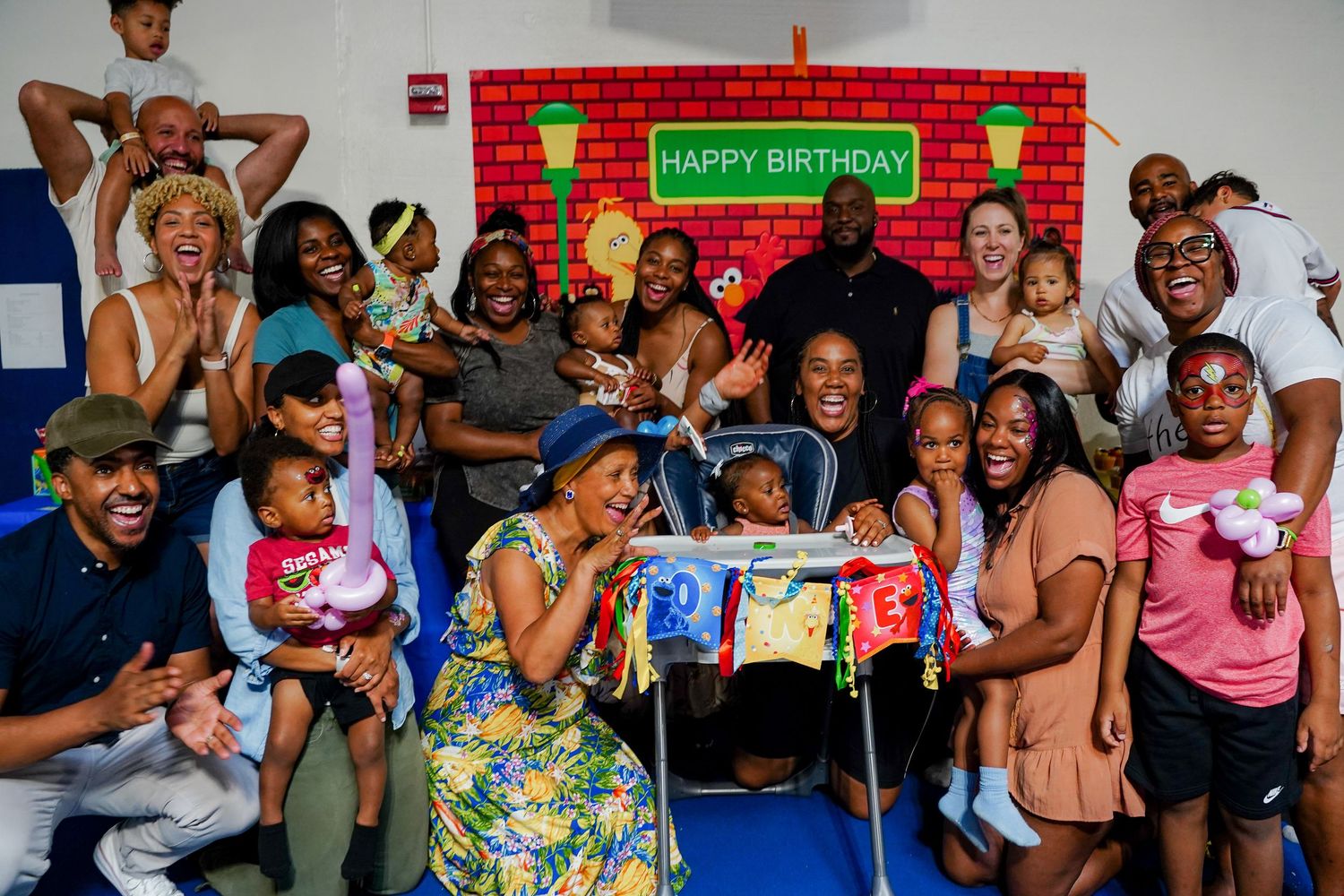 Large joyful family group celebrating a Happy Birthday party with colorful Sesame Street backdrop.