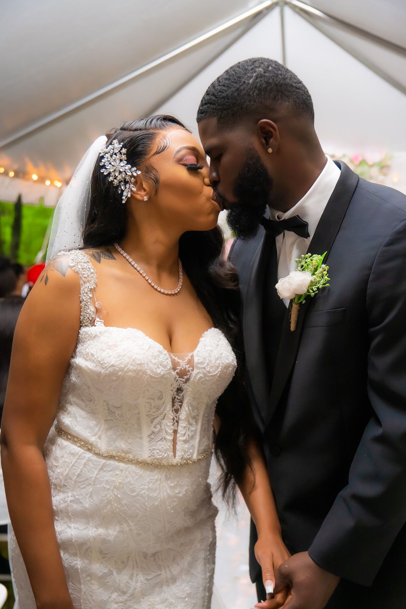 Newlyweds share a romantic kiss, bride in lace gown wearing pearl necklace and hair accessory.